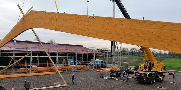 Ein Kran hebt eine massive Holzkonstruktion in die Höhe.