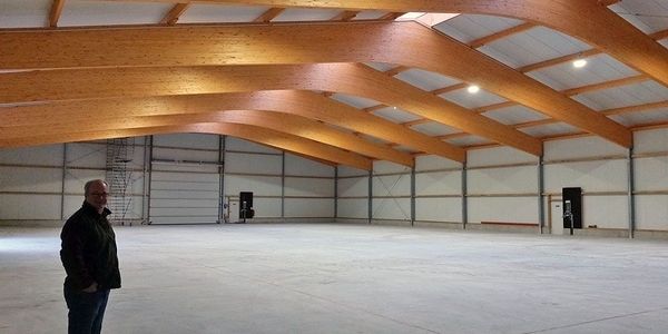 Ein Mann steht in einem leeren Lagerhaus mit Holzträgern, umgeben von weitläufigem Raum und natürlichem Licht.