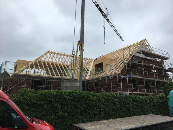 Ein Haus wird mit Holzträgern gebaut, die Struktur ist sichtbar und zeigt den Fortschritt der Bauarbeiten.