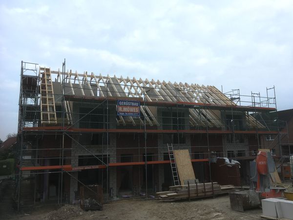 Ein im Bau befindliches Haus mit Gerüst und Holzträgern, das den Fortschritt der Bauarbeiten zeigt.