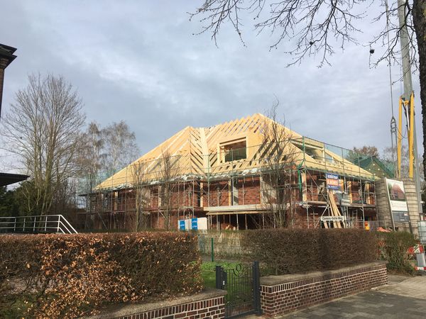Ein Haus wird mit Holzträgern gebaut, das Gerüst ist sichtbar und zeigt den Fortschritt der Bauarbeiten.