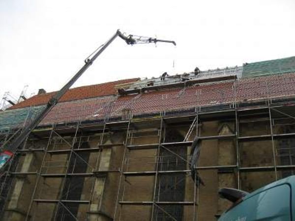 Ein Kran hebt Baumaterialien auf ein im Bau befindliches Dach.