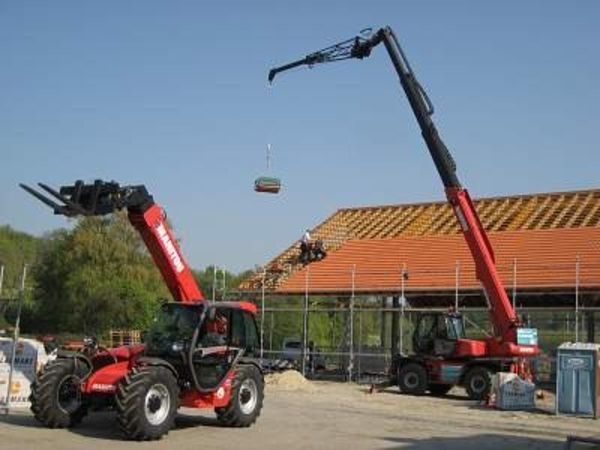 Zwei rote Kräne die vor einen im bau befindliches Haus stehen.