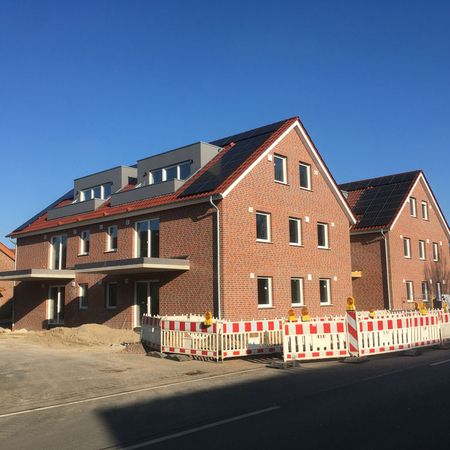 Ein im Bau befindliches Haus auf einer Straße, umgeben von Bauzäunen, die den Baustellenbereich abgrenzen.