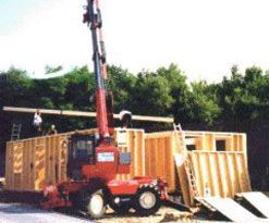 Ein roter Teleskopkrank hebt die Holzbalken am Holzrahmenbau an.