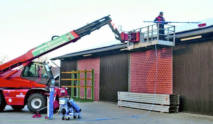 Ein roter Kran mit einer Transportplattform zum reinigen von Photovoltaikanlagen.